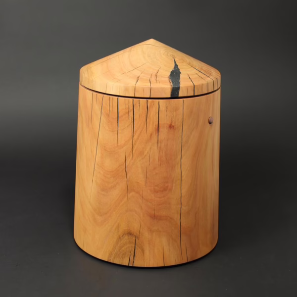 Holzurne in runder Obeliskform mit sich zur Oberseite verjüngendem Kegeldach. Holzart Kirschbaum.